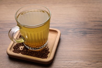 Photo of Cup of aromatic buckwheat tea and granules on wooden table. Space for text