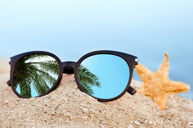 Green palm leaves mirroring in sunglasses on sandy beach with starfish
