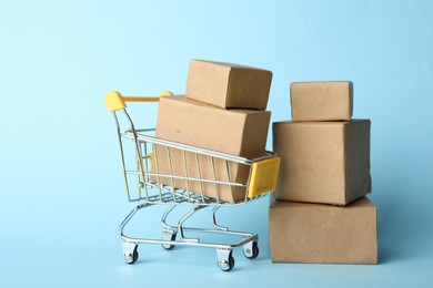 Photo of Shopping cart and boxes on light blue background. Logistics and wholesale concept