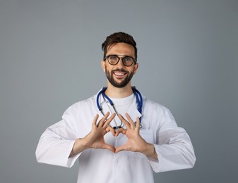 Doctor making heart with hands on grey background