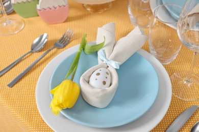 Photo of Festive table setting with painted egg, plate and tulip flower. Easter celebration