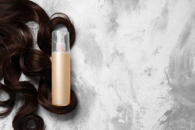 Photo of Spray bottle with thermal protection and lock of brown hair on grey textured background, flat lay. Space for text
