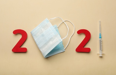 Paper numbers, medical mask and syringe forming 2021 on beige background, flat lay. Coronavirus vaccination