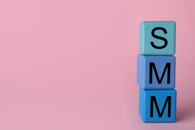 Blue cubes with abbreviation SMM (Social media marketing) on pink background. Space for text