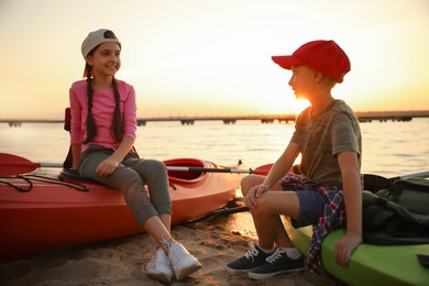 Happy children sitting on kayaks near river at sunset. Summer camp