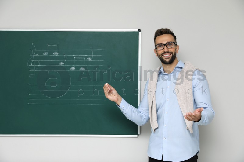 Teacher near green chalkboard with music notes in classroom