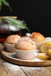 Tasty muffins served with banana slices on wooden table against dark background