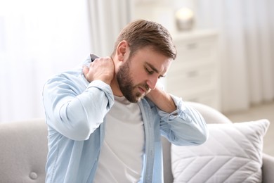 Photo of Man suffering from neck pain at home. Bad posture problem