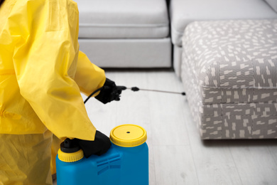 Pest control worker spraying pesticide under furniture indoors, closeup