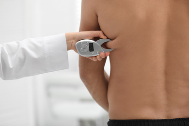 Nutritionist measuring man's body fat layer with digital caliper on blurred background, closeup