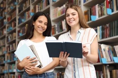 Young women with books near shelves in library