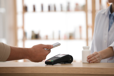 Photo of Customer using terminal for contactless payment with smartphone in pharmacy, closeup
