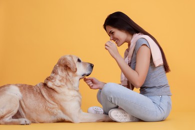 Photo of Happy woman playing with cute Labrador Retriever on orange background