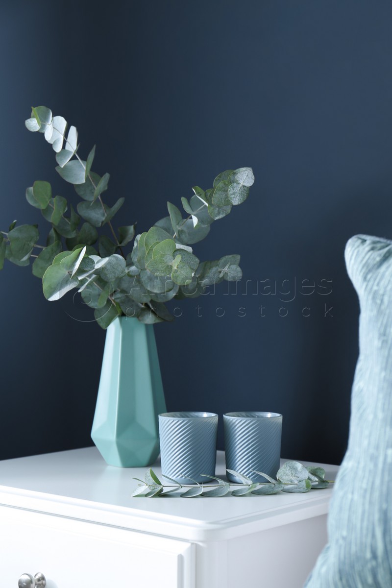 Beautiful eucalyptus branches and candles on white table near blue wall. Interior element