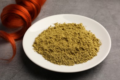 Photo of Henna powder and red strand on light grey table. Natural hair coloring