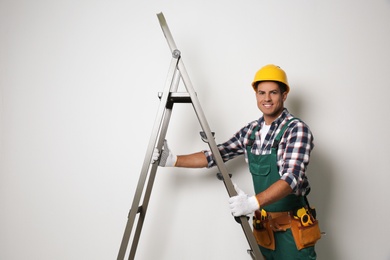 Professional builder with metal ladder on light background