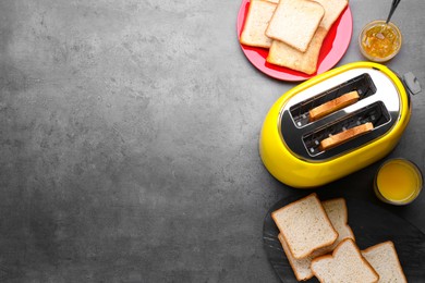Yellow toaster with roasted bread, glass of juice and jam on grey table, flat lay. Space for text
