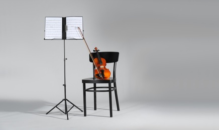 Violin, chair and note stand with music sheets on grey background. Space for text