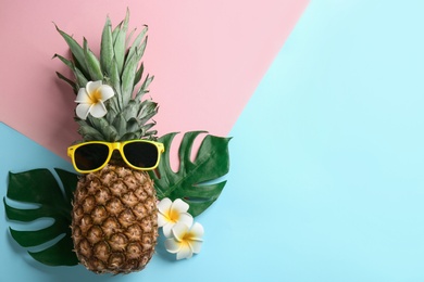 Top view of pineapple with sunglasses, tropical leaves and flowers on color background, space for text. Creative concept