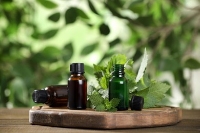 Glass bottles of nettle oil and leaves on wooden table against blurred background, space for text
