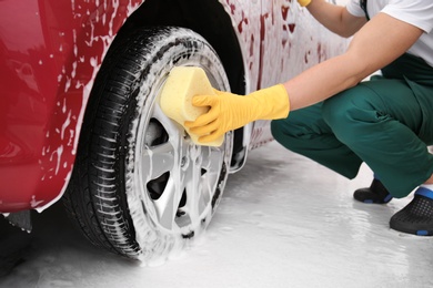 Male worker cleaning vehicle wheel with sponge at car wash