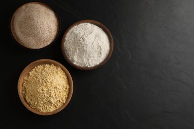 Different types of flours on black table, flat lay. Space for text