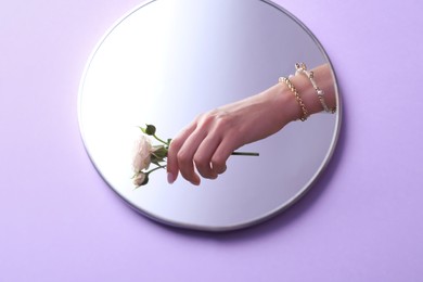 Reflection of woman with beautiful jewelry and flower in mirror on violet background, above view