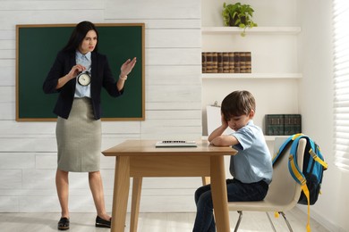 Teacher with alarm clock scolding pupil for being late in classroom
