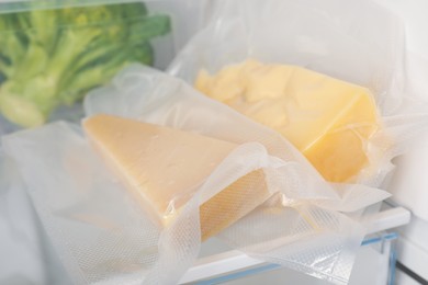 Photo of Vacuum bags with cheese pieces in fridge, closeup. Food storage
