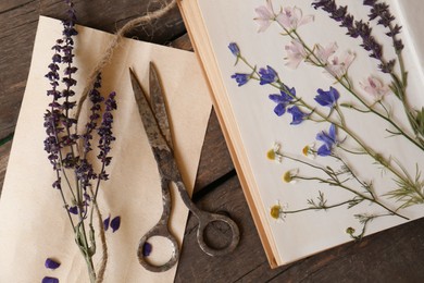Old scissors with beautiful dried flowers and book on wooden table, flat lay