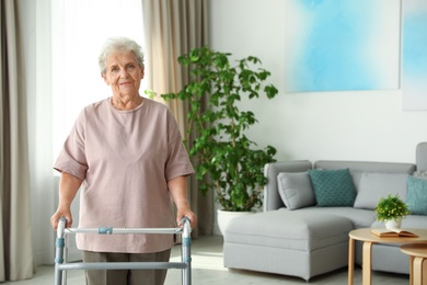 Elderly woman using walking frame indoors. Space for text