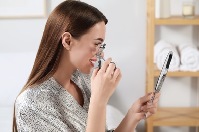 Photo of Woman using eyelash curler near mirror at home