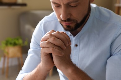 Religious man with clasped hands praying indoors, closeup