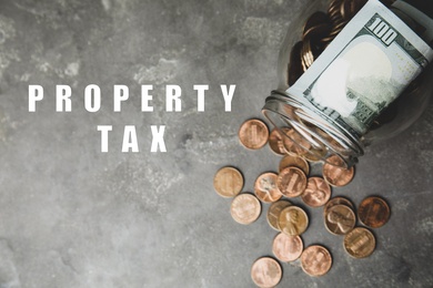 Text Property Tax near jar with dollars and coins on grey table, top view