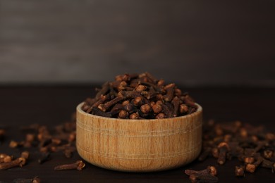 Bowl and aromatic dry cloves on wooden table