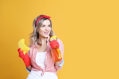 Beautiful young woman with rag and bottle of detergent singing on orange background. Space for text
