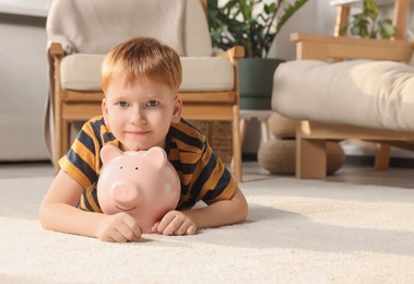 Cute little boy with ceramic piggy bank on floor at home