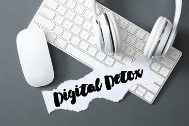 Photo of Paper note with phrase DIGITAL DETOX, headphones and computer devices on grey background, flat lay