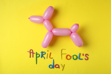 Balloon animal and phrase APRIL FOOL'S DAY on yellow background, flat lay