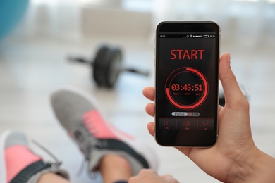 Young woman using fitness app on smartphone indoors, closeup. Space for text