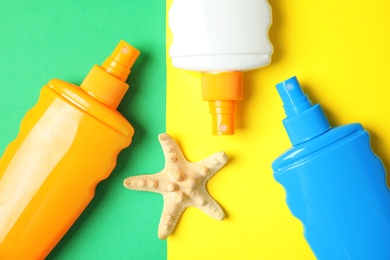 Bottles with sun protection products and starfish on color background, flat lay