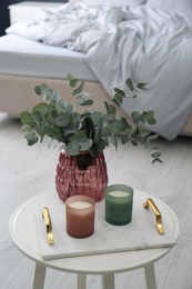 Candles and eucalyptus branches on white table in bedroom. Interior element
