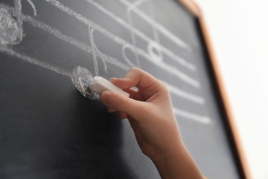 Child writing music notes on blackboard, closeup
