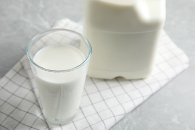 Glass of milk near gallon bottle on light table, closeup
