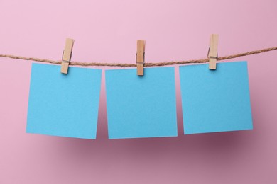 Wooden clothespins with blank notepapers on twine against pink background. Space for text