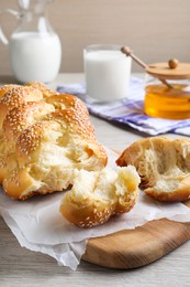 Broken homemade braided bread with sesame seeds on wooden table. Traditional Shabbat challah