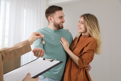 Real estate agent giving key to happy young couple in new house, focus on hands