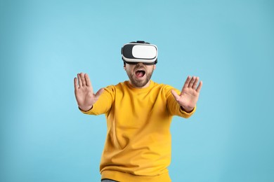 Emotional man using virtual reality headset on light blue background