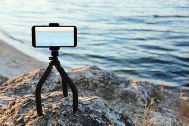 Photo of Tripod with smartphone on rocky river coast. Space for text