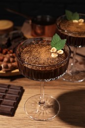 Photo of Dessert bowls of delicious hot chocolate and ingredients on wooden table, closeup